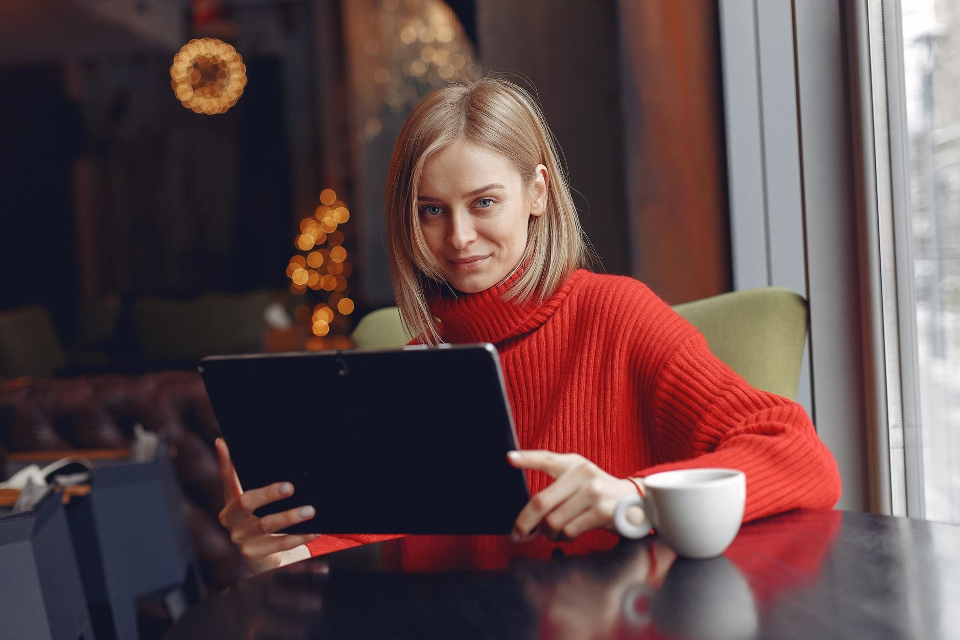Woman reviewing digital content on a tablet with warm cafe light.